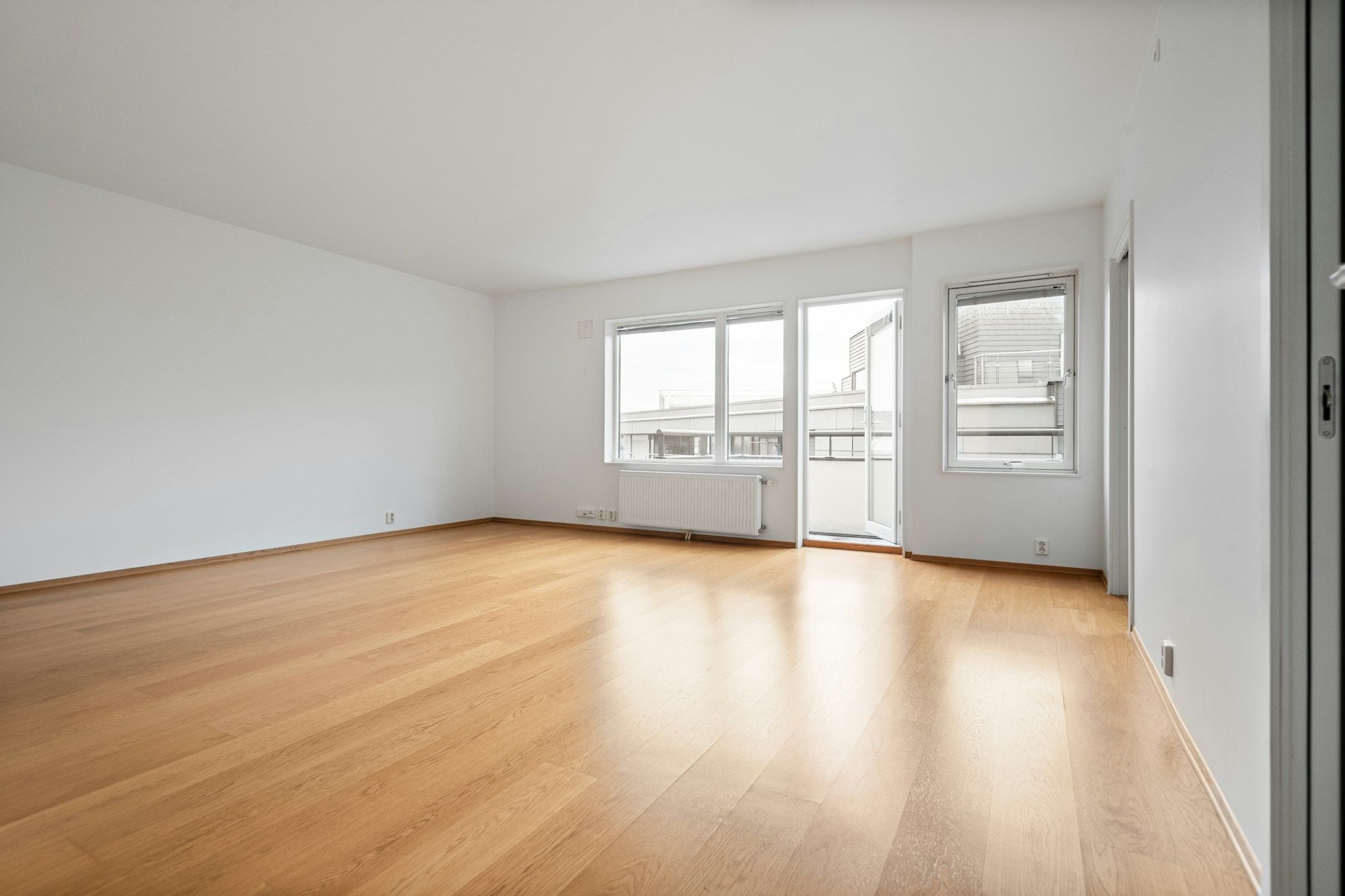 Sala de um apartamento novo, vazia, com piso de madeira e janelas amplas